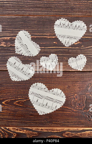 Papier Herzen mit Noten, Ansicht von oben. Weißen herzförmigen Figuren aus Papier auf dunkel strukturierten Hintergrund. Liebe, Musik und Romantik. Stockfoto