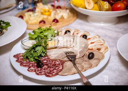 Essen Teller mit leckeren Salami, Schinken, Wurst, Salat und Gemüse. Kalte Fleischplatte. Schneiden von Wurst und Wurstwaren auf einem festlichen Tisch. Buffet mit kalten Snacks Stockfoto