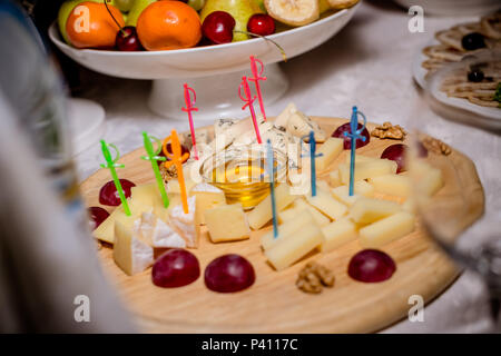 Still-leben Käseplatte mit Nüssen und Trauben. Käseplatte mit Nüssen und Honig serviert. Leckere kalte Vorspeise. Platte mit verschiedenen Sorten von Brie, Blau- und Parmesan. Buffet mit kalten Snacks Stockfoto