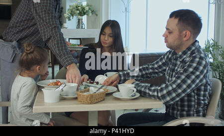 Kellner bringen Pasta zu wenig hübsche Mädchen, das Abendessen mit ihrer Familie in ein Restaurant. Ihre Eltern haben aßen ihre Salate. Stockfoto