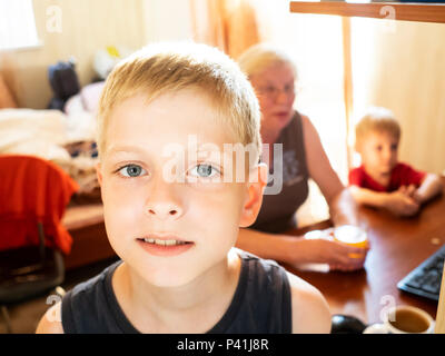 Ein 10-jähriger Weißer Junge vor dem Hintergrund seiner Großmutter posing und jüngerer Bruder sitzen, die durch das Steuergerät Stockfoto