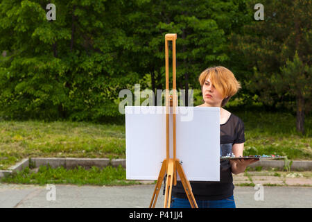 Künstler junge Frau malt auf einer Leinwand eine Stadtlandschaft im Sommer von Ölfarben im City Park Stockfoto