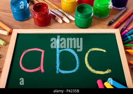 ABC in Farbe Kreide auf einer kleinen elementaren Tafel mit verschiedenen Farben, Kreiden und Stifte auf der Schulbank geschrieben. Stockfoto