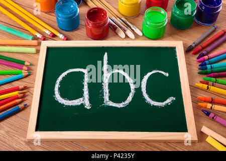 ABC mit Kreide auf einer kleinen elementaren Tafel mit verschiedenen Farben, Kreiden und Stifte auf der Schulbank geschrieben. Stockfoto