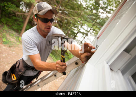 Ein Bauarbeiter hämmerten einen Nagel Vinylabstellgleis in Ontario, Kanada zu sichern. Stockfoto