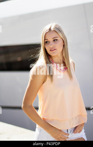 Hübsches blondes Mädchen zu Fuß auf einem Pier tief in mit einem Schiff im Hintergrund gedacht Stockfoto