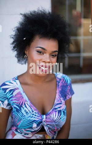 Ein afrikanisches Modell wirft, während an einem Tisch in einem floralen Crop Top sitzen Stockfoto