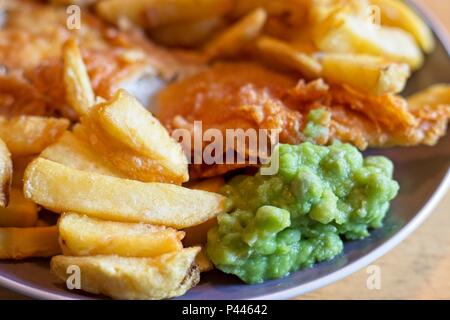 Fisch und Chips, eine traditionelle englische Mahlzeit bestehend aus Frittierter Kabeljau und Chips mit Erbsenpüree Stockfoto