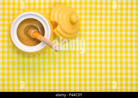 Ein Bienenstock themed Topf voll Manuka Honig mit hölzernen Löffel gelb kariertem Hintergrund mit kopieren. Stockfoto