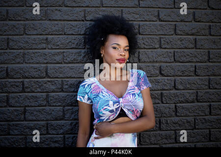 Eine junge südafrikanische Modell steht mit ihrem Arm über ihren Bauch gegen eine dunkel gestrichene Wand Stockfoto