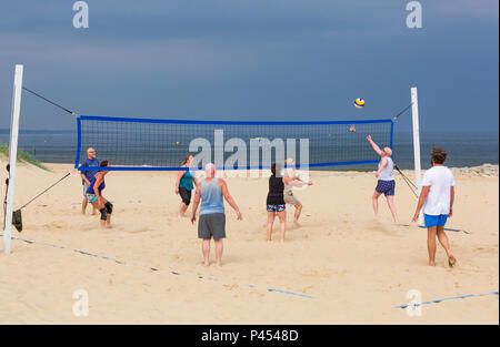 Die Leute, die Spaß am Beachvolleyball am Strand Sandbänke unter Dunkelgrau stürmischen Himmel, Poole, Dorset im Mai Stockfoto