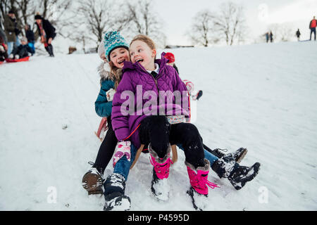 Drei kleine Mädchen sitzen auf einem Schlitten zusammen, Bergabfahren im Schnee. Stockfoto