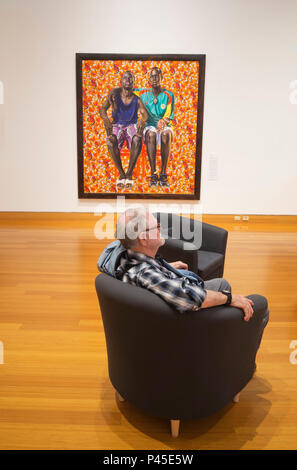 Malerei 'Dogon Paar" von zeitgenössischen afroamerikanischen Künstler Kehinde Wiley auf Anzeige. Man Relaxen im Stuhl mit Malerei in den Hintergrund. Stockfoto
