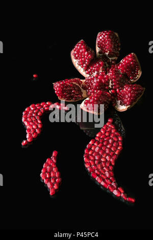 Kunst Präsentation der geöffneten reifer Granatapfel mit Samen als Kurven auf schwarzem Hintergrund reflektiert angeordnet. Stockfoto