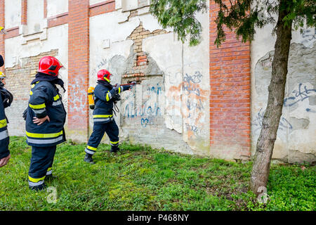 Ansicht von hinten auf Feuerwehrmann in Uniform mit voller Schutzausrüstung, mit Brecheisen die Mauer durchbrechen. Stockfoto