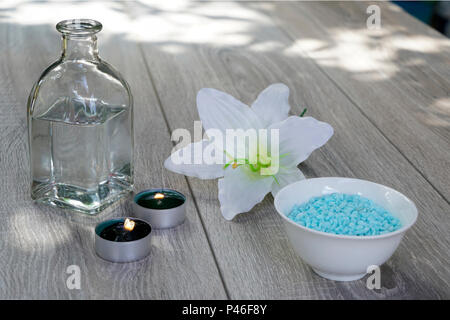 Eine Flasche, weiße Blüten, Badesalz und Kerzen, Entspannung im Freien auf einer hölzernen Tisch... Stockfoto