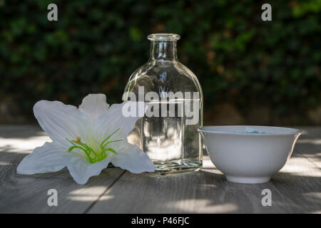 Eine Flasche, weißen Blüten und Badesalz, Entspannung im Freien auf einem Holztisch. Stockfoto