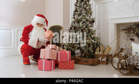 Santa Claus insgeheim anbringen Geschenkboxen unter dem Weihnachtsbaum Stockfoto