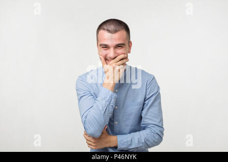 Close up Portrait des jungen Mannes lachen und über seinen Mund mit der Hand über weißen Hintergrund. Versuchen, ein Lachen zu halten, nicht irgendeine Person zu beleidigen. Er j Stockfoto