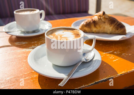 Zwei Tassen belebender Cappuccino und ein Croissant zum Frühstück Stockfoto