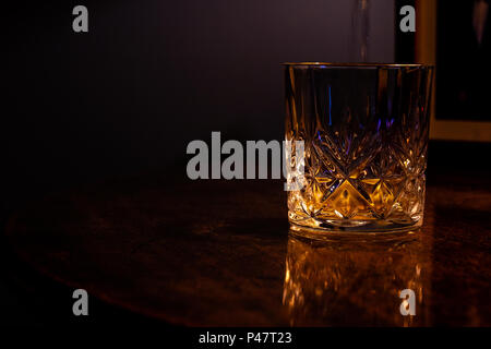 Whiskey in einem Kristall Glas auf ein dunkles gemasertes Tabelle gegossen Stockfoto
