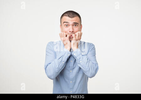Portrait ängstlichen jungen Mann im blauen Hemd Beißen seiner Nägel Finger heraus freaking. Er hat Angst, die Ergebnisse der Untersuchung oder Nachrichten hören. Stockfoto