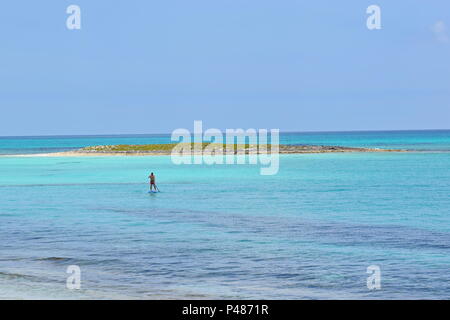 Mann in weiter Ferne auf dem Paddleboard im bunten blauen Wasser der Bahamas Stockfoto