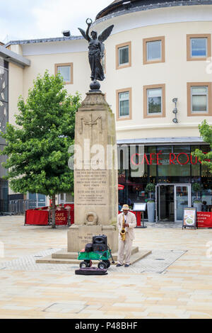 Gaukler spielen ein Saxophon vom War Memorial in Jubilee Square outside cafe Rouge, Stadtzentrum von Woking, Surrey, Südosten, England, Grossbritannien Stockfoto