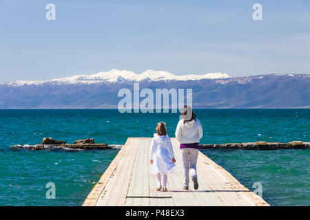 Ohrid, Republik Mazedonien: Kinder gehen auf einem Pier am Ohrid See mit schneebedeckten Bergen im Hintergrund. Stockfoto