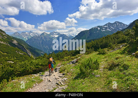 Radfahrer reiten Mountainbike Downhill in üppig-grünen Natur. Rocky Mountains und blauer Himmel mit Wolken im Hintergrund. Tirol, Österreich Stockfoto