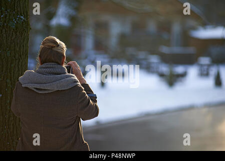 Über die Schulter geschossen von einer Frau Fotografieren von einem zugefrorenen See im Winter Sonnenschein Stockfoto