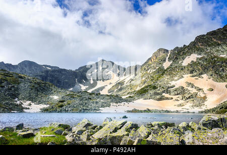 Rila Mountain Lake und lichtdurchfluteten Mussala Gipfel auf einer schneebedeckten Landschaft mit Vordergrund Felsen Stockfoto