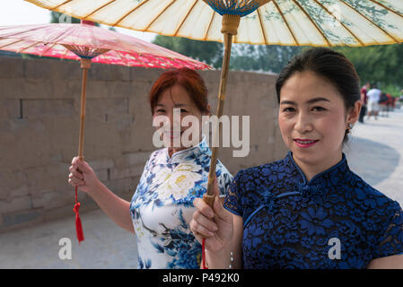 Zwei reife Frauen Akteure in traditionellen eng anliegende Kleider tragen Papier Sonnenschirme Besucher begrüßen, Dong E E Jiao Stadt Liaocheng, Stockfoto