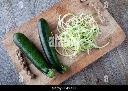 Blick von oben auf die zwei Zucchini auf einer hölzernen Schneidebrett mit einem Stapel von Zucchini Spaghetti Stockfoto