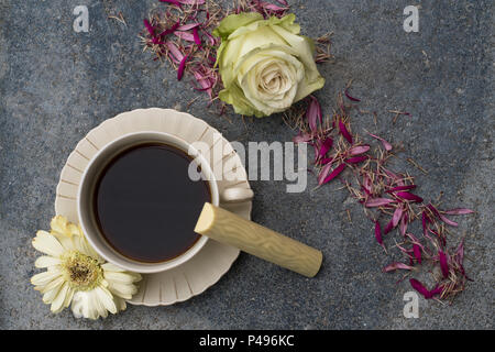 Eine Tasse mit Kaffee steht vor der dunklen konkreten Hintergrund. Champagnerfarbenen Blüten und Blumen Blüten das Bild schmücken. Eine Süßigkeit aus weißem Stockfoto