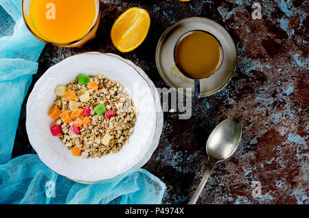 Gesundes Frühstück mit hausgemachtem Müsli in weiße Platte mit farbigen kandierte Früchte, Kaffee und Orangensaft auf dunklem Hintergrund. Kopieren Sie Platz Stockfoto