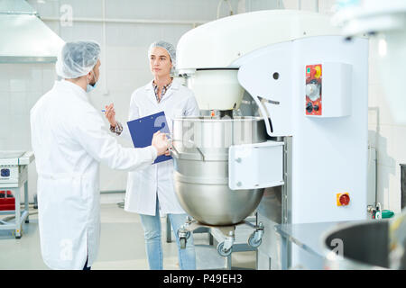 Zwei Konditoren ständigen Gespräch in der Nähe von Maschinen im Werk Stockfoto
