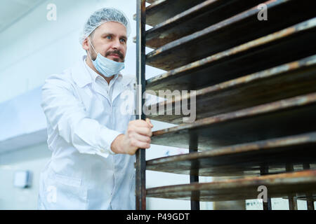 Mann im weißen Uniform beweglichen Regalen für Brot Stockfoto