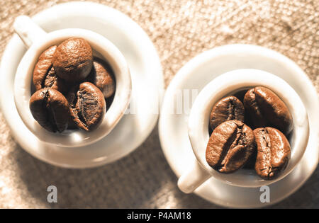 Kaffeebohnen in einer schönen kleinen Porzellan Tassen close-up. Starker Kaffee Poster. Stockfoto