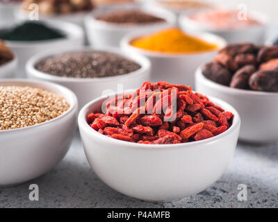 Goji Beeren in der kleinen weißen Schale und andere superfoods für den Hintergrund. Selektive konzentrieren. Verschiedene superfoods Zutaten. Konzept und Grafik für superfood und entgiftende Lebensmittel Stockfoto