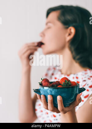 Frische reife Erdbeere Mädchen in einem hellen Kleid ist eine blaue Schüssel mit Erdbeeren Nahaufnahme Stockfoto