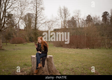 Frau mit Handy beim Sitzen auf Baumstumpf Stockfoto