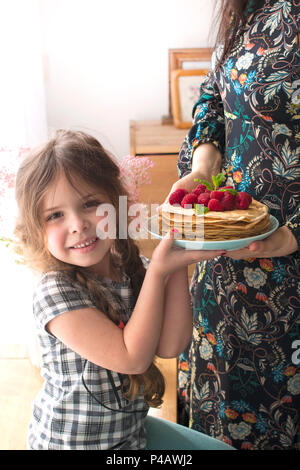 Mom und das Mädchen halten einen Teller mit hausgemachten Pfannkuchen und Beeren. Köstliches Frühstück zu Hause. Eine glückliche Familie. Guten Morgen. Stockfoto