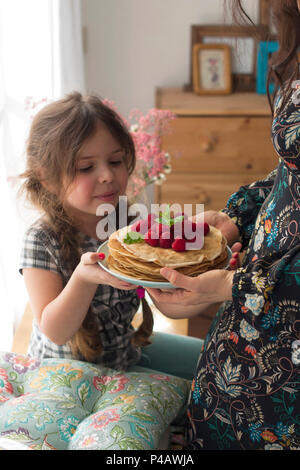 Mom und das Mädchen halten einen Teller mit hausgemachten Pfannkuchen und Beeren. Köstliches Frühstück zu Hause. Eine glückliche Familie. Guten Morgen. Stockfoto