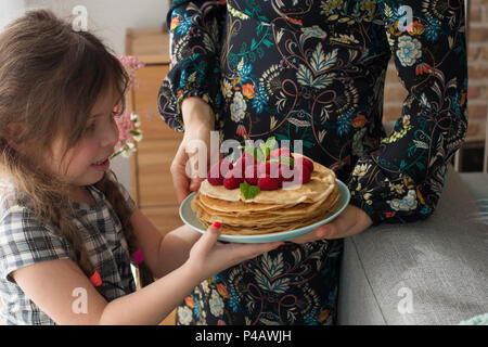 Mom und das Mädchen halten einen Teller mit hausgemachten Pfannkuchen und Beeren. Köstliches Frühstück zu Hause. Eine glückliche Familie. Guten Morgen, Stockfoto