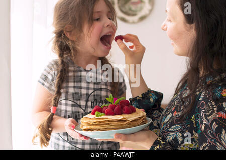 Mom und das Mädchen halten einen Teller mit hausgemachten Pfannkuchen und Beeren. Köstliches Frühstück zu Hause. Eine glückliche Familie. Guten Morgen, Stockfoto