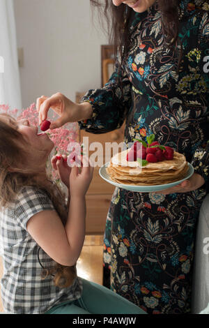 Mom und das Mädchen halten einen Teller mit hausgemachten Pfannkuchen und Beeren. Köstliches Frühstück zu Hause. Eine glückliche Familie. Guten Morgen Stockfoto