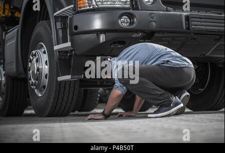 Problem mit Defekten Lkw, kaukasische Trucker in seinem 30s für Schäden unter seinem Fahrzeug suchen. Automobil- und Transportindustrie Thema. Stockfoto