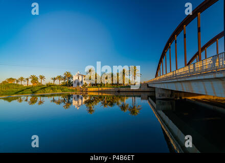 Blick auf eine Kirche mit einem Spiegelbild im Wasser und eine Brücke über den Fluss in der Region Alboraya. Valencia, Spanien. Stockfoto