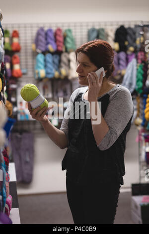 Frau auf der Suche nach Garn während Gespräch am Handy Stockfoto